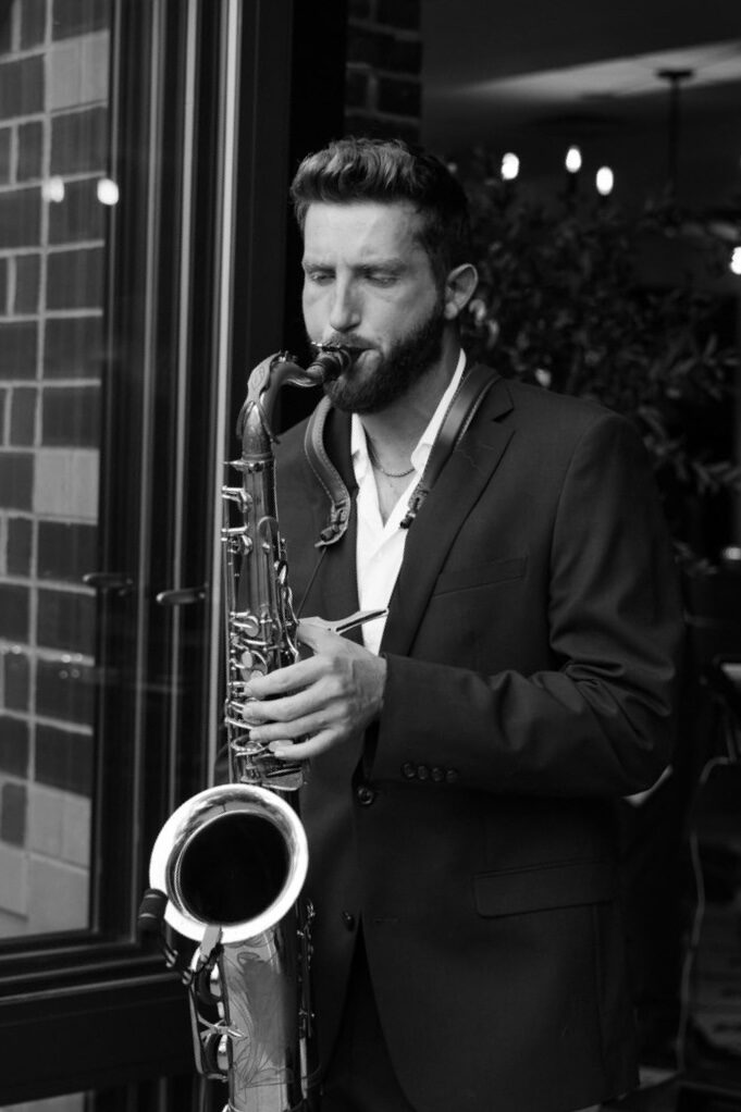 Dawson Bertrand performing live saxophone in a black suit at a restaurant patio, black and white
